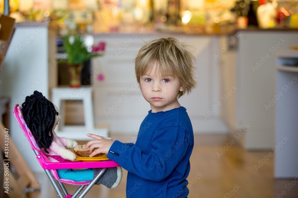 Little toddlerchild, boy, feeding his favorite doll, sitting in doll chair Little toddlerchild, boy, feeding his favorite doll, sitting in doll chair