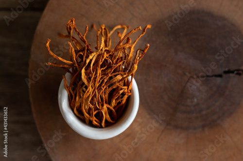 Dry cordyceps militaris in a white bowl with wooden background. Orange medical mushroom for good health. photo