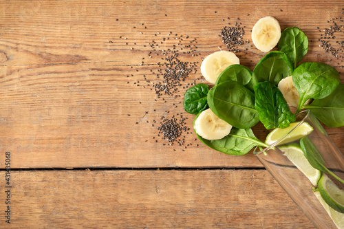 Healthy food concept. Ingredients for cooking detox smoothie. Glass with spinach, banana, lime and chia seeds on wooden table top view, copy space