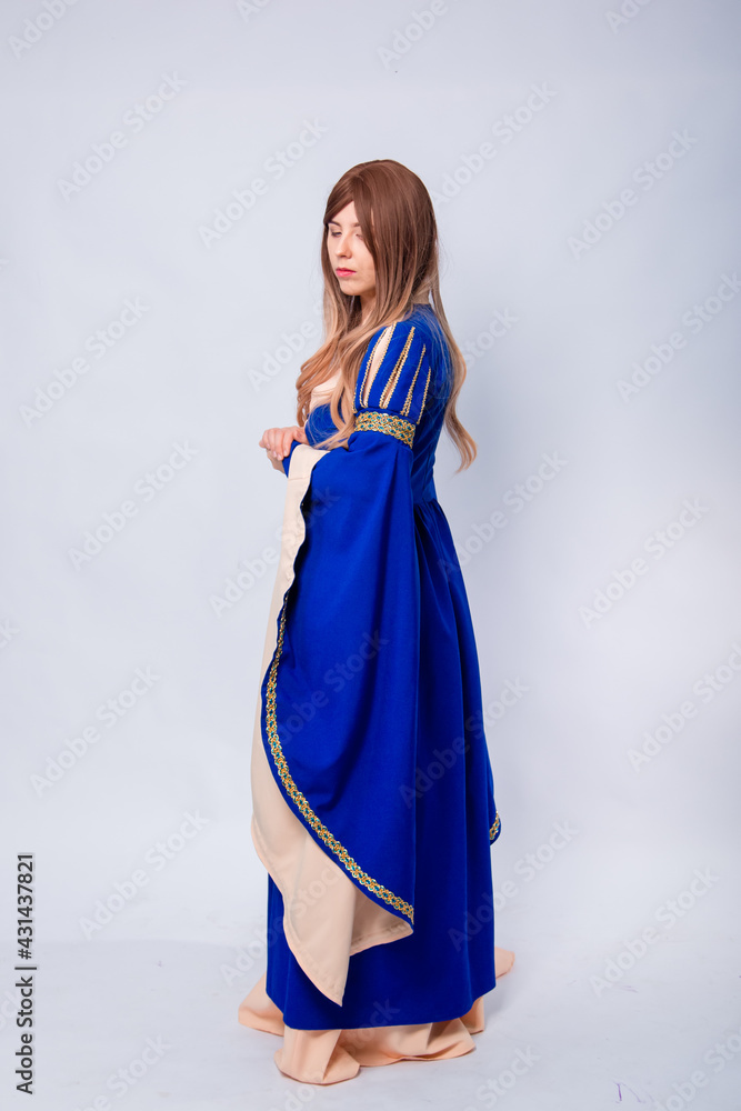 A full-length portrait of an attractive woman with long hair in a medieval, fantasy, blue and beige dress with long, large sleeves, posing isolated on a white background. A full-length portrait of an attractive woman with long hair in a medieval, fantasy, blue and beige dress with long, large sleeves, posing isolated on a white background.