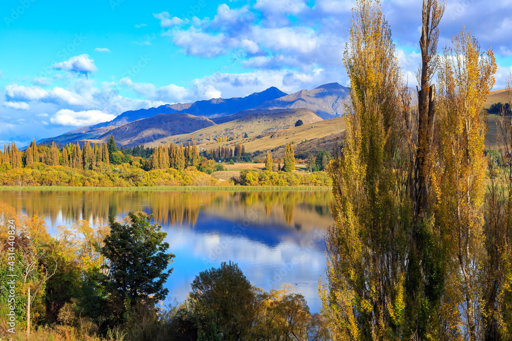 Lake Hayes in the South Island of New Zealand. Autumn trees and mountains are reflected in the lake's tranquil waters 