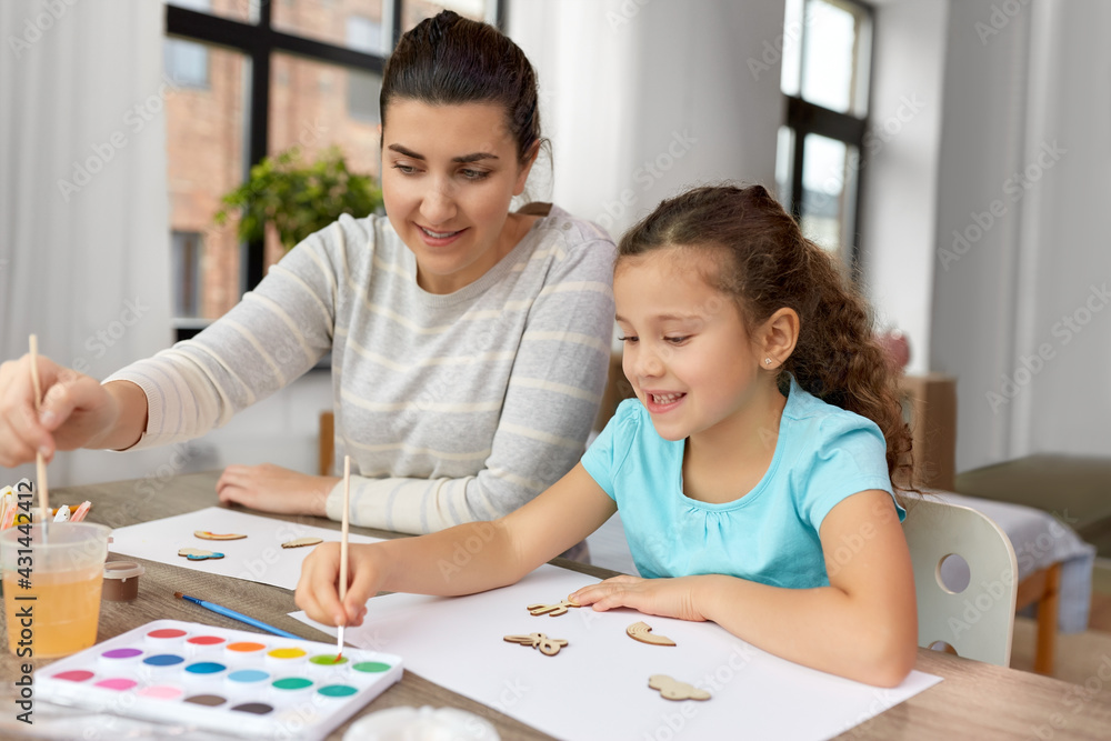 family, hobby and leisure concept - happy smiling mother spending time with her little daughter drawing or painting wooden chipboard items with colors at home family, hobby and leisure concept - happy smiling mother spending time with her little daughter drawing or painting wooden chipboard items with colors at home