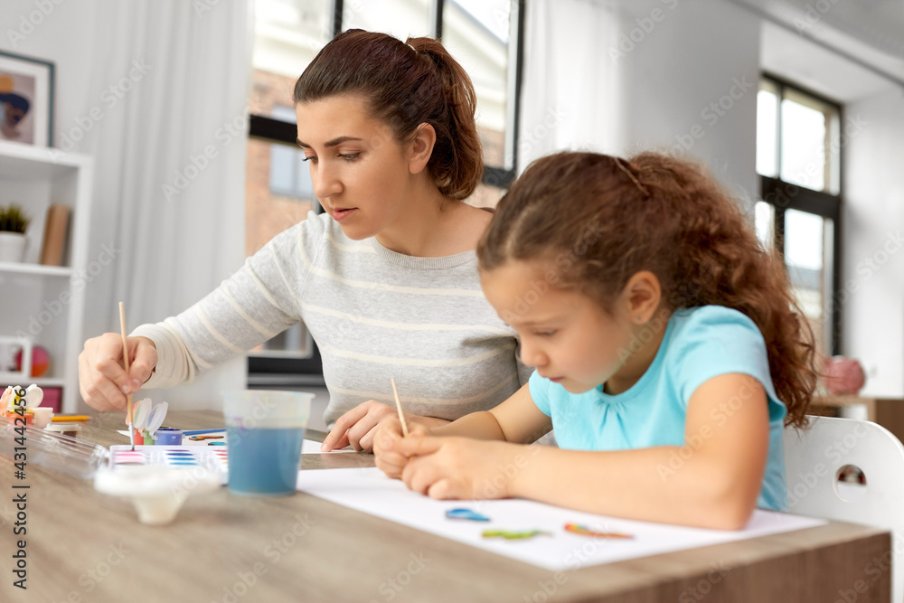 family, motherhood and leisure concept - mother spending time with her little daughter drawing or painting wooden chipboard items with colors at home family, motherhood and leisure concept - mother spending time with her little daughter drawing or painting wooden chipboard items with colors at home