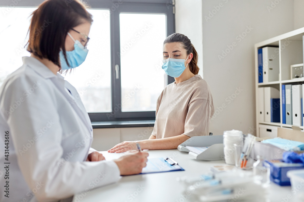 medicine, healthcare and pandemic concept - female doctor in medical protective mask or nurse with clipboard and patient at hospital medicine, healthcare and pandemic concept - female doctor in medical protective mask or nurse with clipboard and patient at hospital