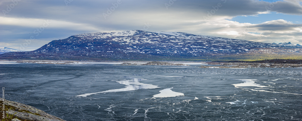 Panoramic image of a landscape in spring with the half frozen reservoir Akkajaure and mountains in Sarek National Park under overcast sky, Lapland, Sweden. Panoramic image of a landscape in spring with the half frozen reservoir Akkajaure and mountains in Sarek National Park under overcast sky, Lapland, Sweden.