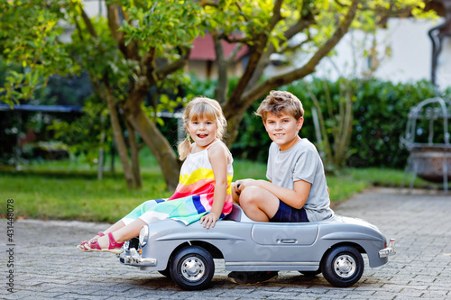 Two happy children playing with big old toy car in summer garden, outdoors. Kid boy pushing and driving car with little toddler girl, cute sister inside. Laughing and smiling kids. Lovely family © Irina Schmidt