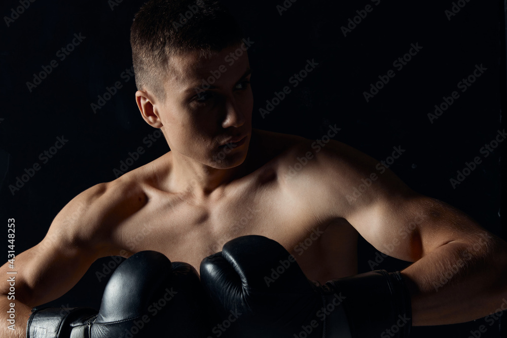 muscular boxer in black gloves on a dark background looking to the side cropped view