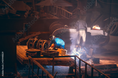 Worker welding metal parts at metallurgical plant, processing metal after casting.