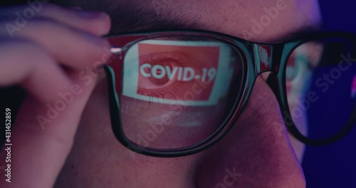 Close-up portrait of man in eyeglasses late at night scrolling news abous coronavirus in front of laptop, macro shot photo