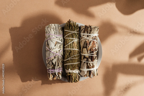 White sage, cedar, yerba santa tied in a bunch on a concrete plate. Set of incense for fumigation, beautifully lit by sunlight. Top view. Close-up color photo. Background with shadow.