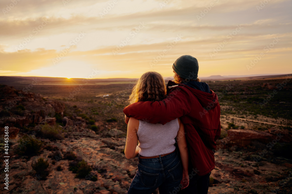 Rear view of young couple enjoying together watching beautiful sunrise standing on mountain