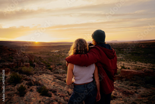 Rear view of young couple enjoying together watching beautiful sunrise standing on mountain