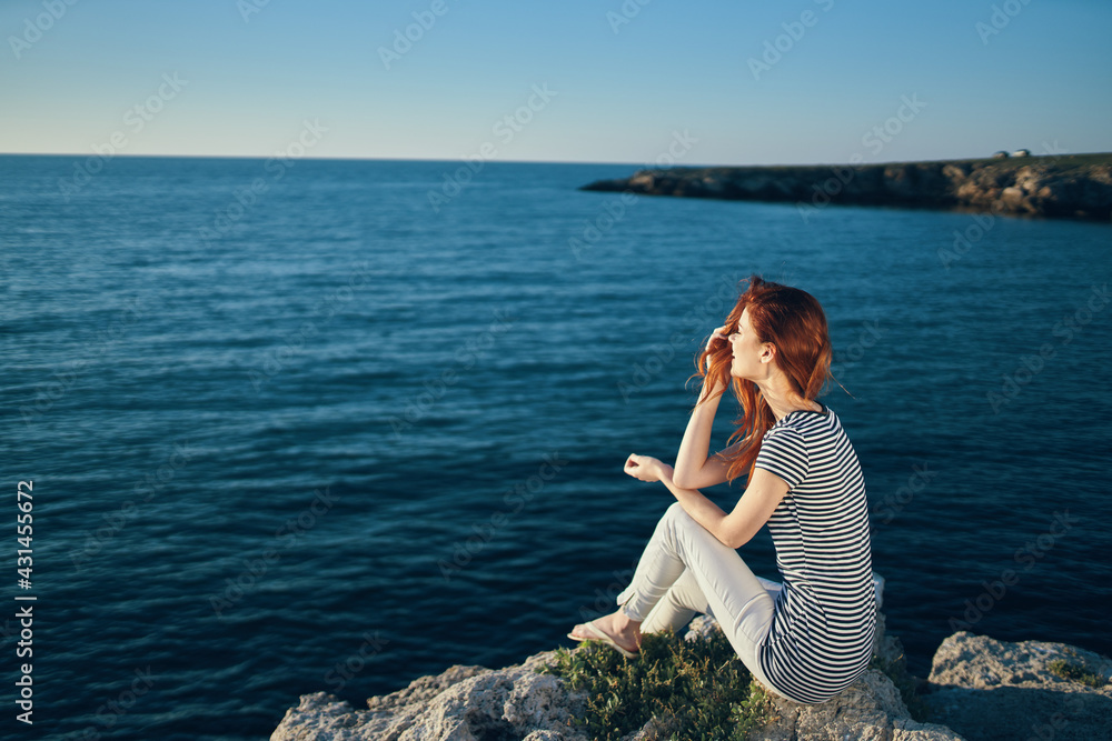 woman in a t-shirt and trousers sits on a rock on the beach near the sea top view
