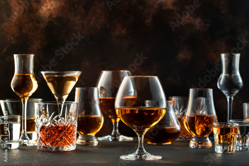 Hard strong alcoholic drinks, spirits and distillates in glasses in assortment: vodka, cognac, scotch, whiskey etc. Brown bar counter background