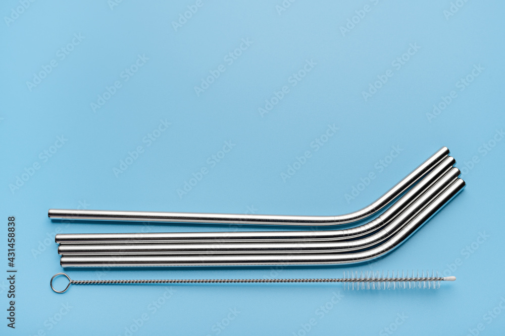 Reusable metal drink straws and cleaning tool on blue background with copy space. Close-up, studio shot.