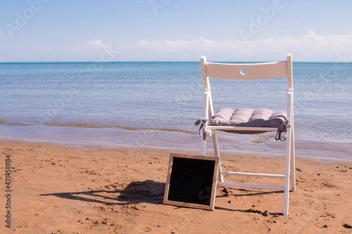 Fototapeta Naklejka Na Ścianę i Meble -  a white chair stands on the seashore, next to it is an empty black plaque in a frame