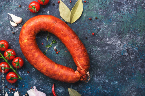 Smoked sausage circle on blue kitchen table with spices, tomatoes and garlic, natural organic meat product, top view, copy space