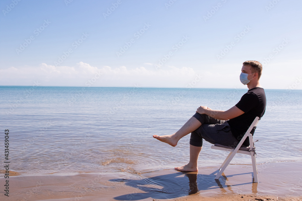 a guy in a blue medical sits on a white chair by the sea