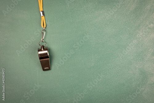 Metal whistle with yellow cord on a green chalk board © STOATPHOTO