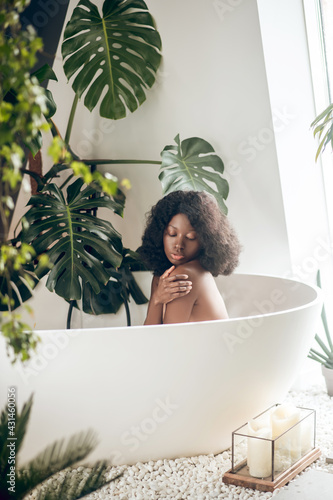 Fotografie Dark-skinned woman relaxing in a bath and washing her body