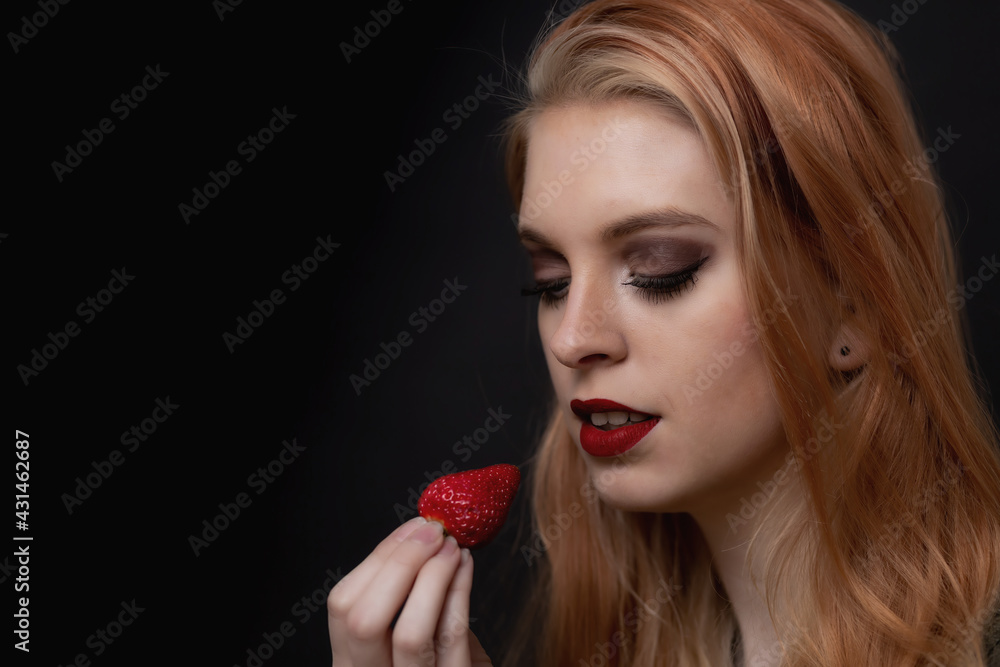 Low key portrait of beautiful long hair young woman posing with fresh strawberry closeup. Horizontally. Low key portrait of beautiful long hair young woman posing with fresh strawberry closeup. Horizontally.