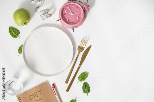 Composition with cutlery, empty plate, measuring tape, diet plan, apple and alarm clock on white background, diet concept photo