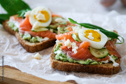Open sandwich traditional danish smorrebrod salmon, cucumber, boiled egg, soft cheese. Homemade sandwich with rye bread on white background, top view. Tasty salmon fish sandwich closeup