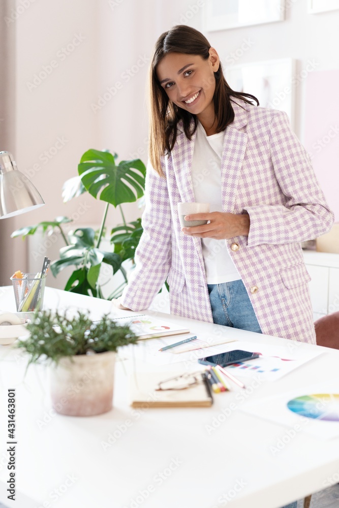 Confident young woman in smart casual wear smiling while standing near her working place Confident young woman in smart casual wear smiling while standing near her working place