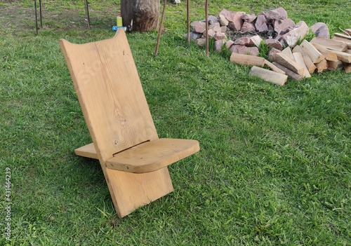 A chair made of two boards. Antique chair. Homemade viking chair, wooden mini chair, two parts only. Green grass background, barn.