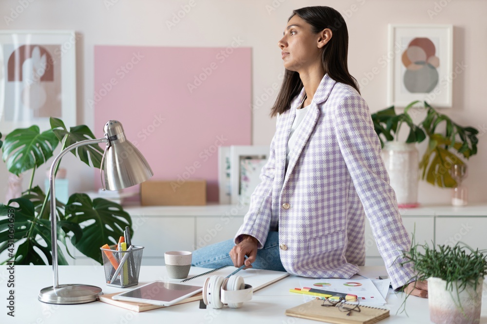Confident young woman in smart casual wear smiling while standing near her working place Confident young woman in smart casual wear smiling while standing near her working place