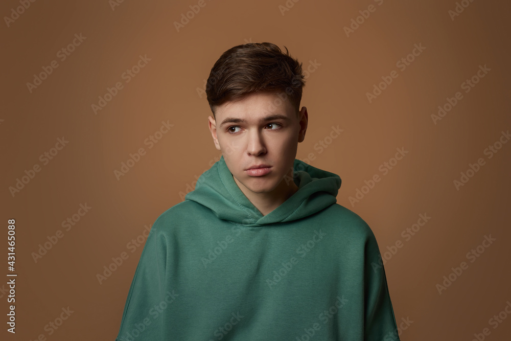 upset young guy in sweatshirt isolated on brown background. upset young guy in sweatshirt isolated on brown background.