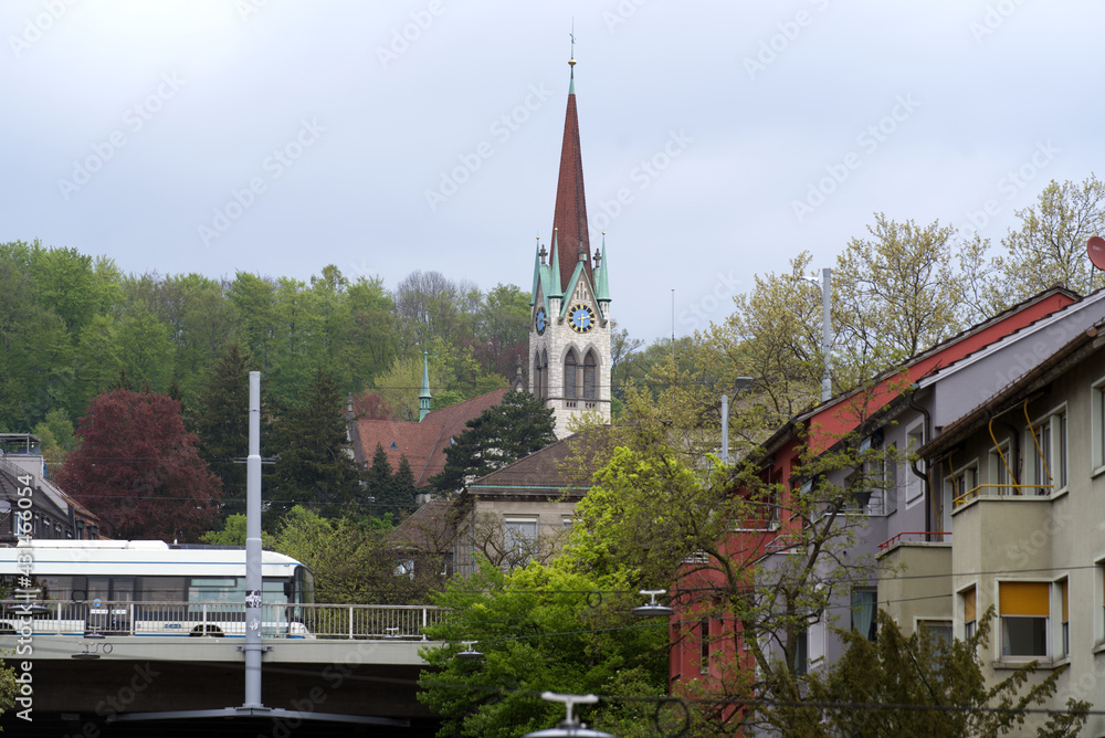 Protestant church of Wipkingen at City of Zurich with trolleybus in the foreground and forest in the background. Photo taken April 29th, 2021, Zurich, Switzerland.