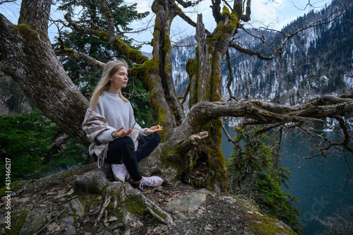 Girl sits on a tree and meditates near lake Ritsa in Abkhazia