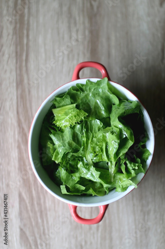 Bowl of lettuce on wooden table. Flat lay.