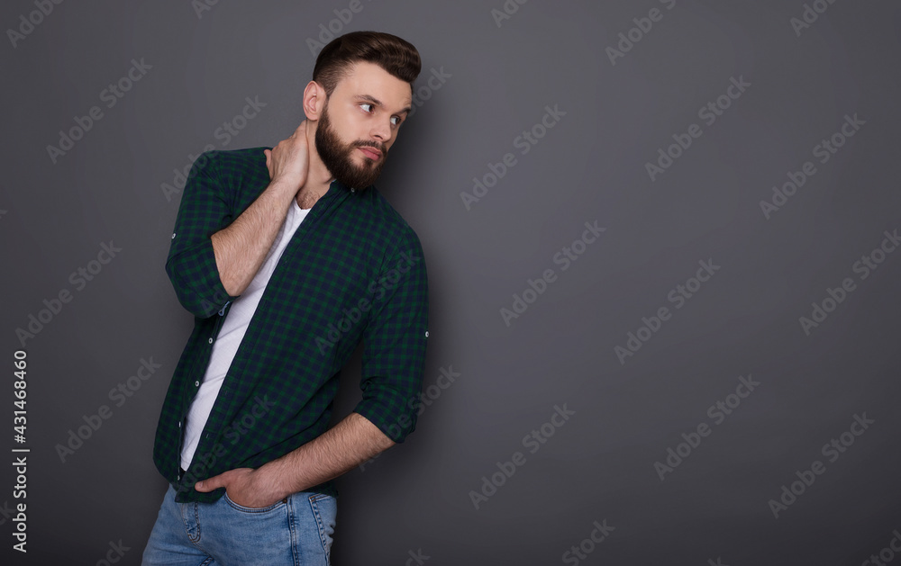 Stylish handsome trendy fashion bearded man in denim wear is posing over gray background in the studio