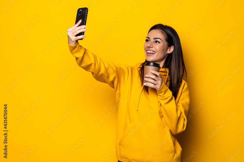 Young woman doing selfie shot on mobile phone isolated on yellow wall background. Young woman doing selfie shot on mobile phone isolated on yellow wall background.