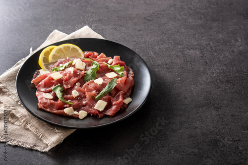 Marbled beef carpaccio on black plate on black stone. Copy space