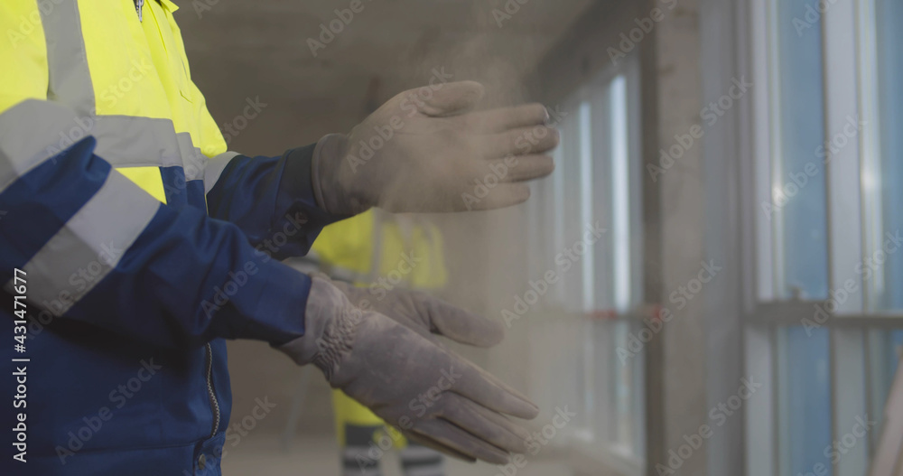 Close up of builder shaking off dust from gloves at construction site Close up of builder shaking off dust from gloves at construction site