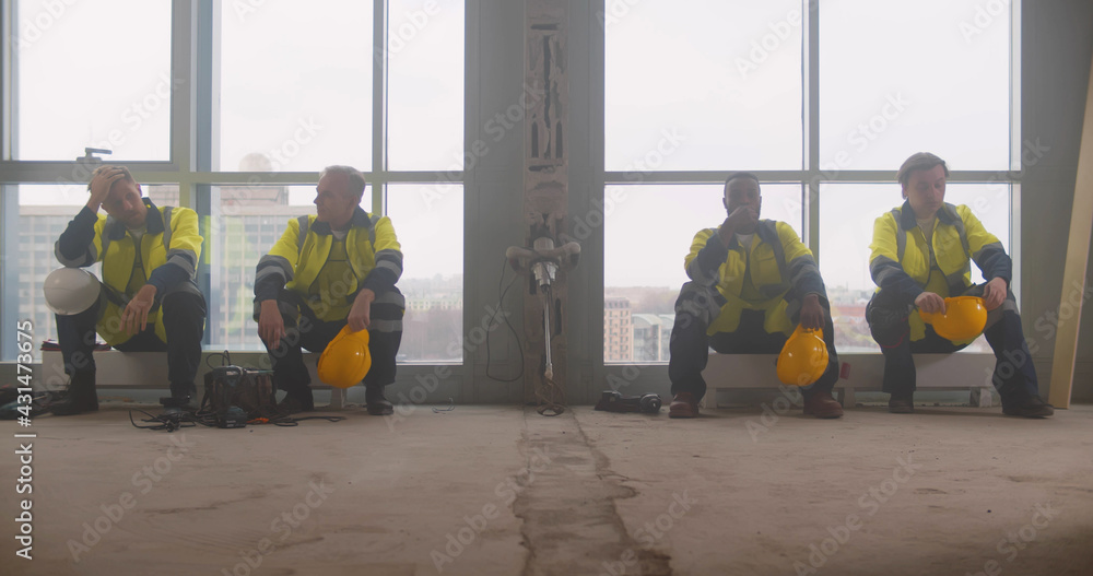 Tired team of builders sitting on heaters and resting at construction site Tired team of builders sitting on heaters and resting at construction site