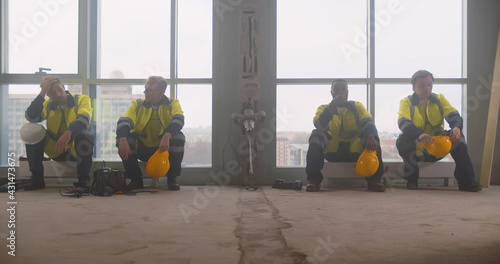 Tired team of builders sitting on heaters and resting at construction site