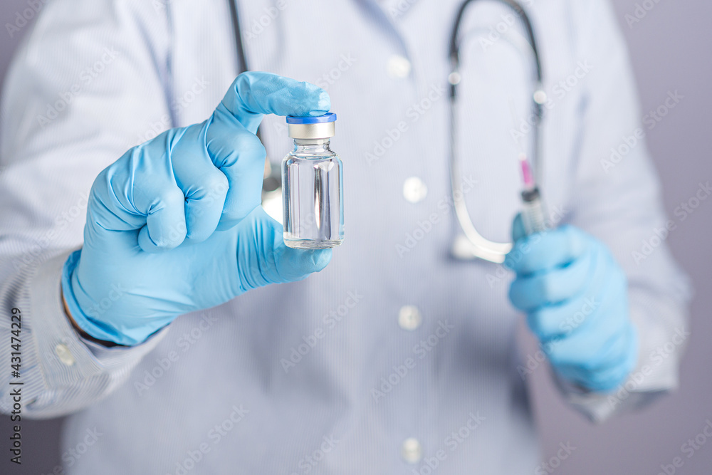 Doctor hand holding of a vaccine bottle and syringe against a gray background. Vaccine for immunization, and treatment from virus infection. Concept of medical and the fight against the virus Doctor hand holding of a vaccine bottle and syringe against a gray background. Vaccine for immunization, and treatment from virus infection. Concept of medical and the fight against the virus