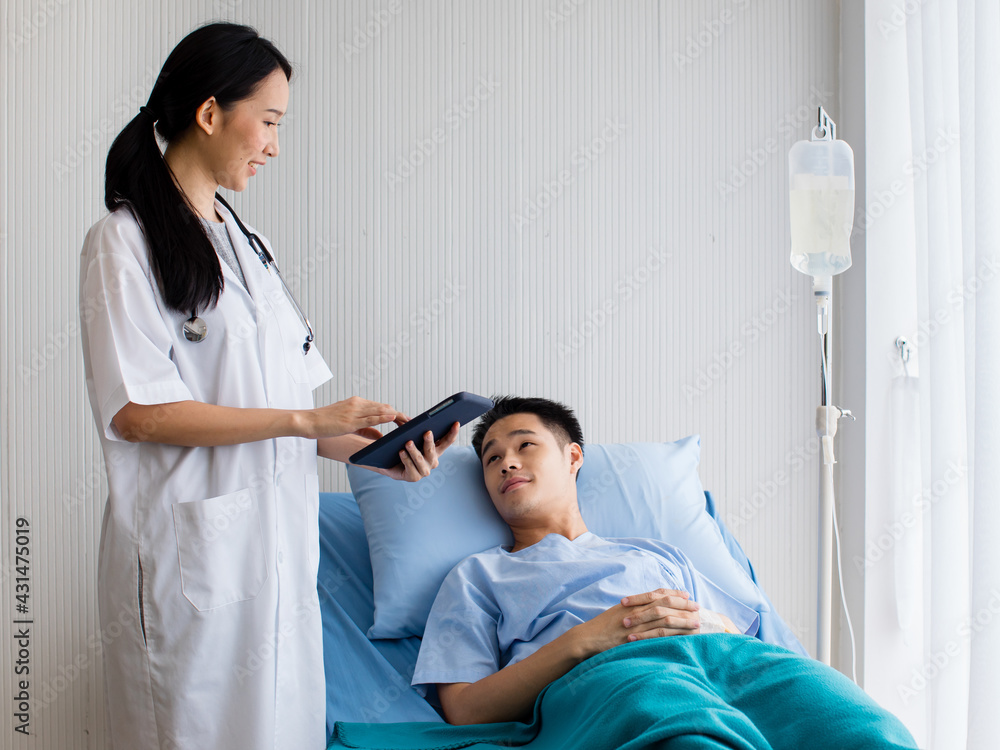 In hospital private room, One female doctor with stethoscope and laptop in her hands talking with patient man as he laying on bed with IV tube. Look each other with smile. Seems guy recovery soon. In hospital private room, One female doctor with stethoscope and laptop in her hands talking with patient man as he laying on bed with IV tube. Look each other with smile. Seems guy recovery soon.