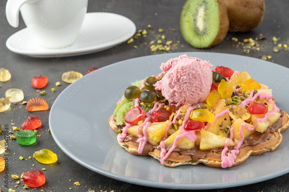 Heart waffle with kiwi and pineapple with gummy candy and ice cream on it. Heart waffle with kiwi and pineapple with gummy candy and ice cream on it.