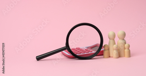 wooden figurines of little men family, magnifier and calculator on a pink background