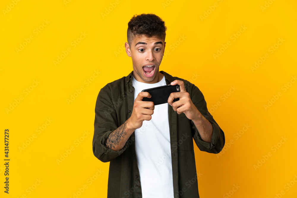 Young brazilian man isolated on yellow background playing with the mobile phone Young brazilian man isolated on yellow background playing with the mobile phone