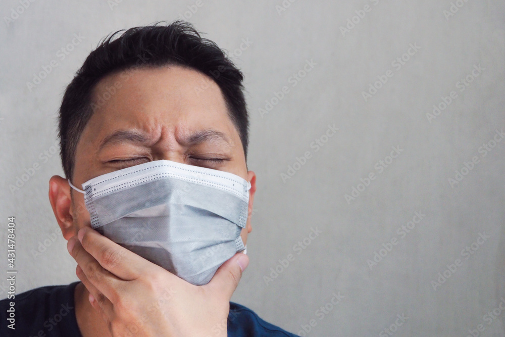 Young Asian man wearing face mask using his hand touching his face feeling painful and sick at home Covid-19 pandemic and human healthcare concept Young Asian man wearing face mask using his hand touching his face feeling painful and sick at home Covid-19 pandemic and human healthcare concept