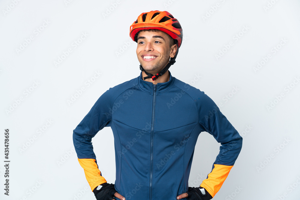 Young cyclist Brazilian man isolated on white background posing with arms at hip and smiling - obrazy, fototapety, plakaty 