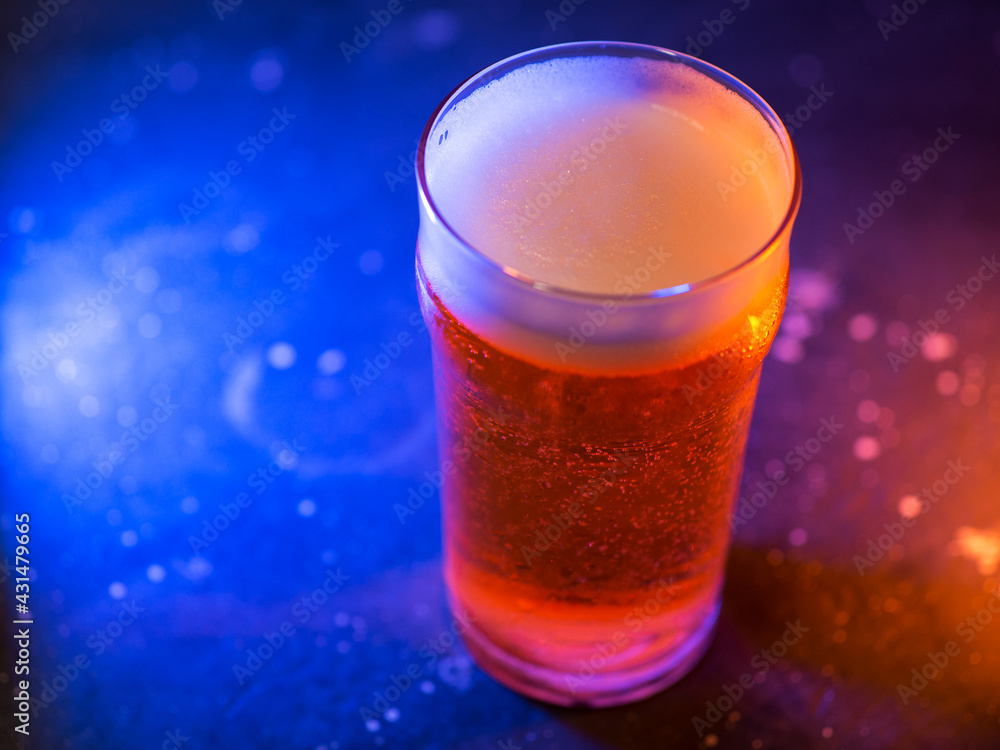 A glass of craft light beer on a dark background, colored trend light A glass of craft light beer on a dark background, colored trend light