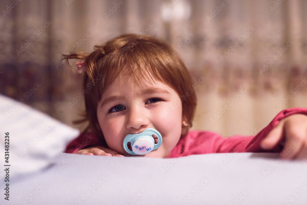a little girl with a pacifier posing in her room. a little girl with a pacifier posing in her room.