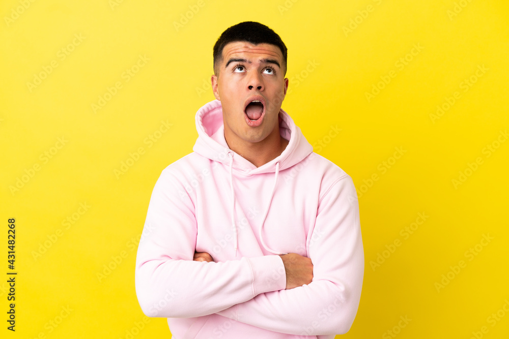Young handsome man over isolated yellow background looking up and with surprised expression Young handsome man over isolated yellow background looking up and with surprised expression